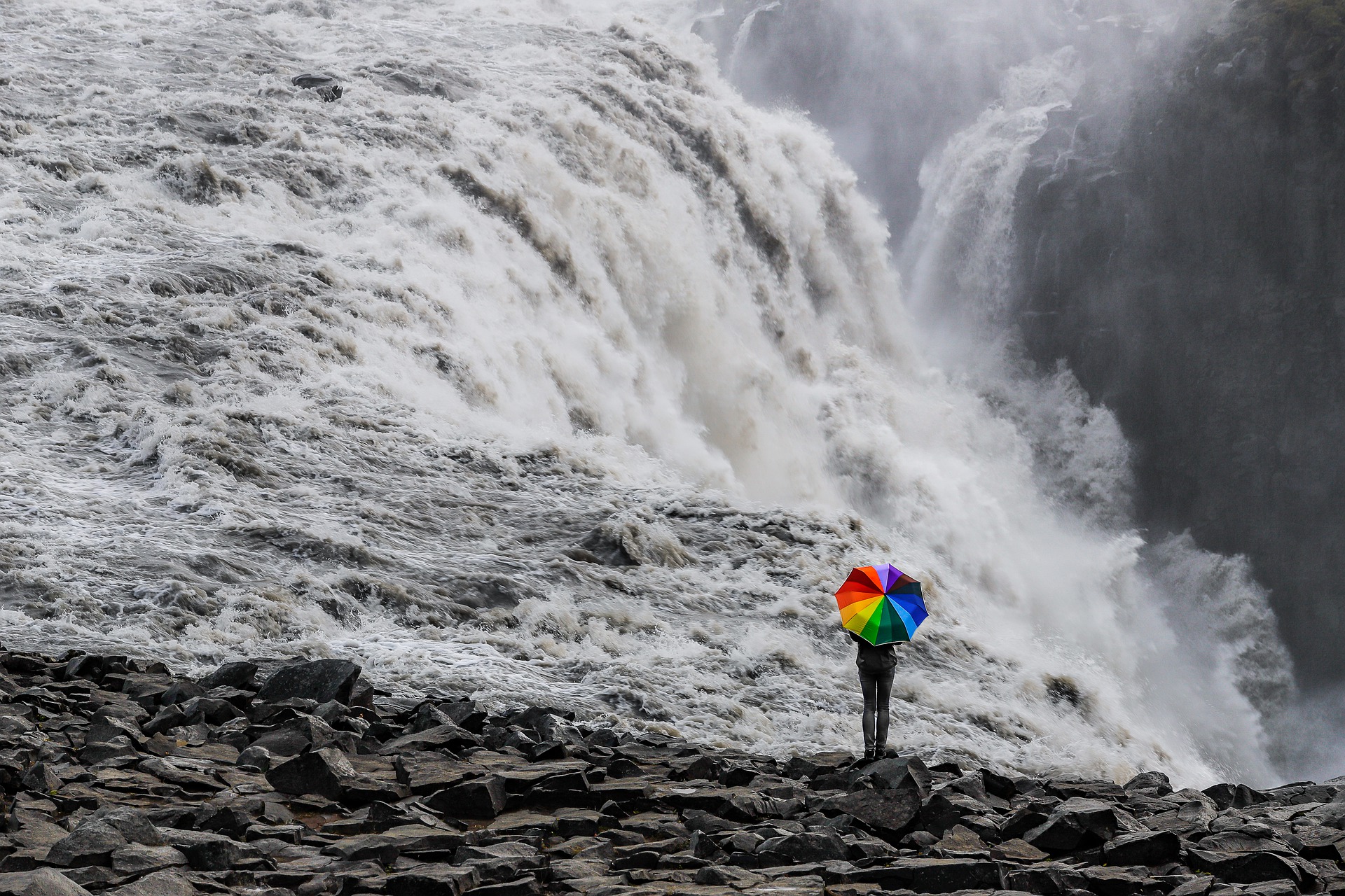 a person with an umbrella looking at dettifoss waterfall in iceland