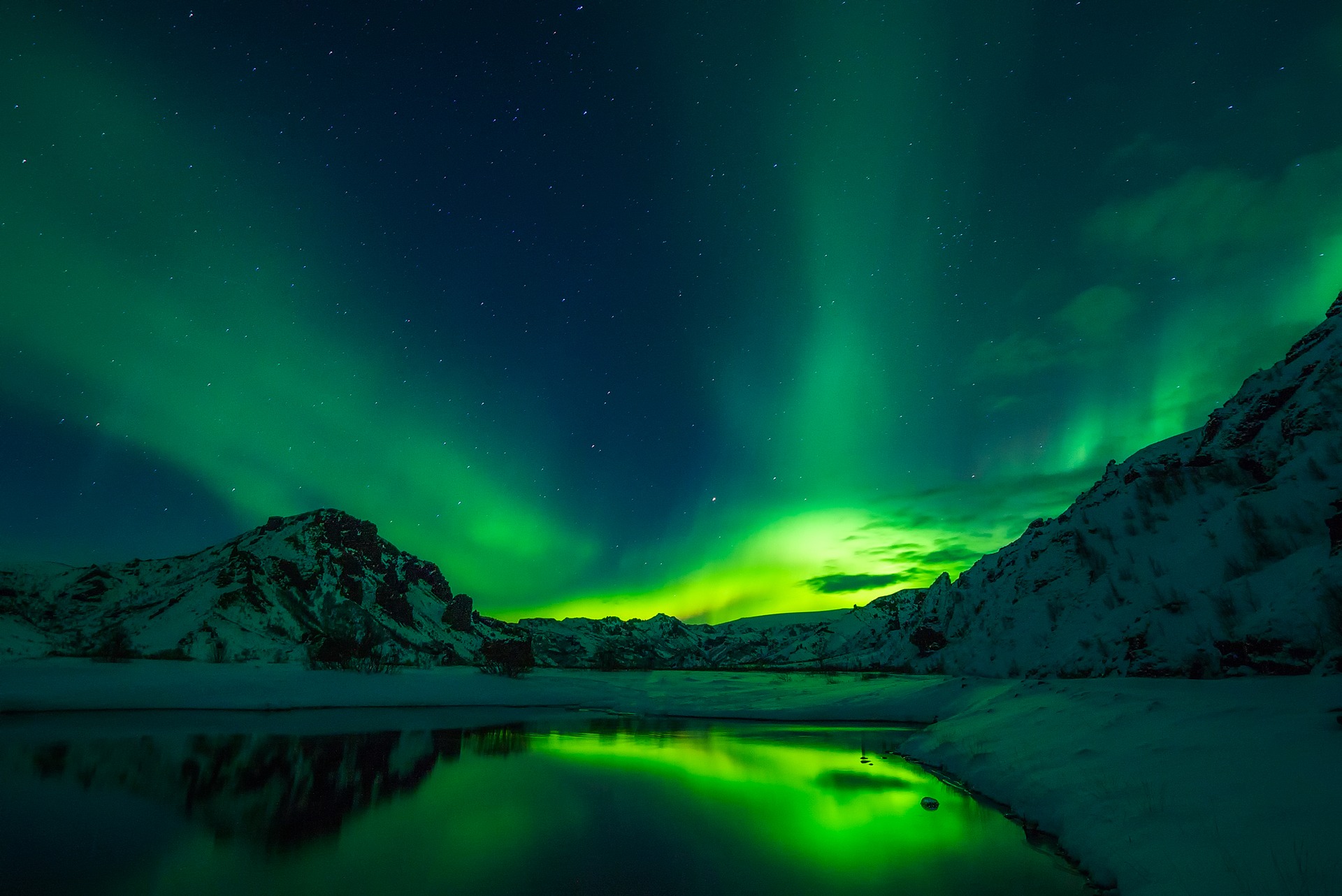 green northern lights above mountains and a lake in iceland