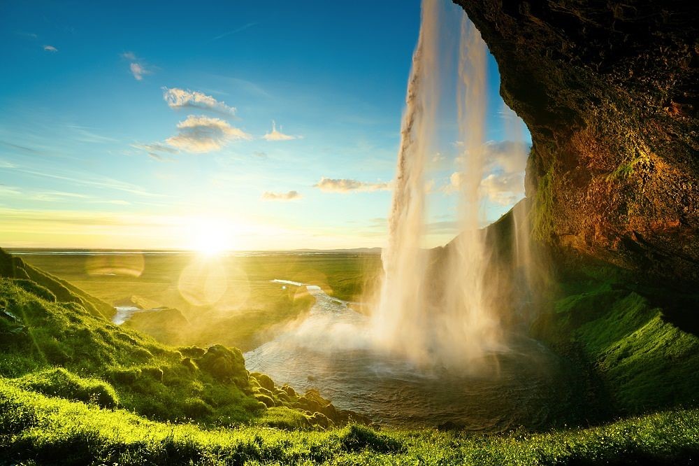 seljalandsfoss waterfall in Iceland with the sun, viewed from behind the falling water