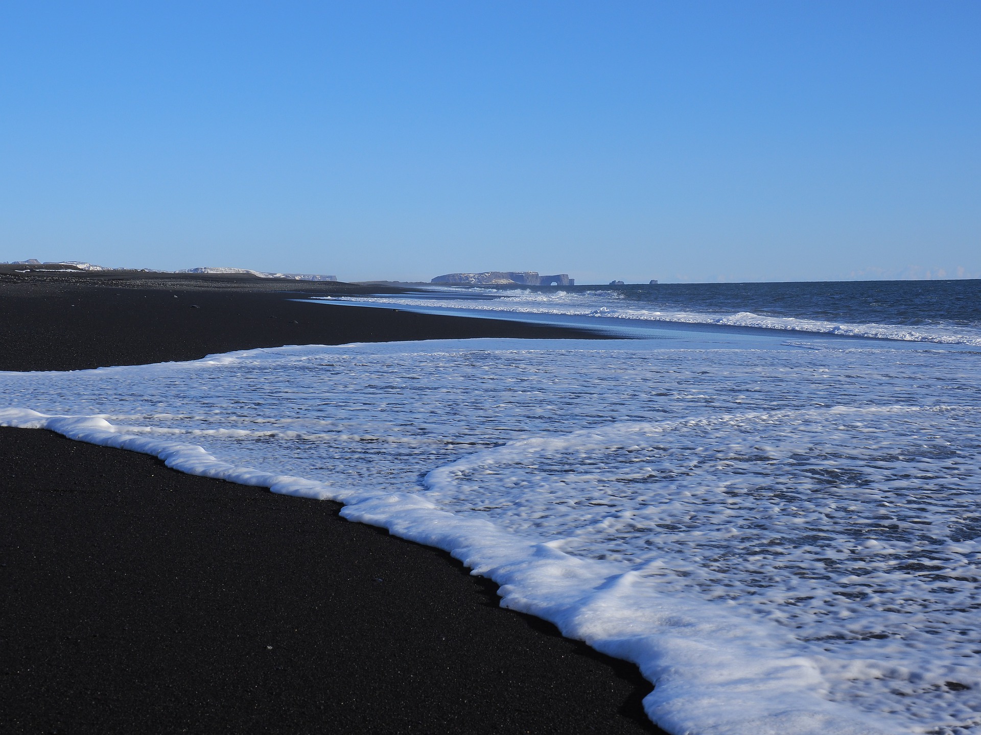 Black Sand Beach of Solheimasandur, black sand and waves with Dyrhoaley on the background