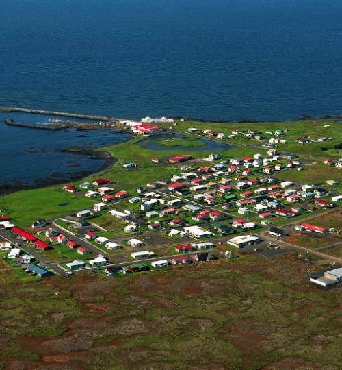 Panoramablick auf das charmante Städtchen Grindavík und die Küste, mit bunten Häusern und Meer im Hintergrund.