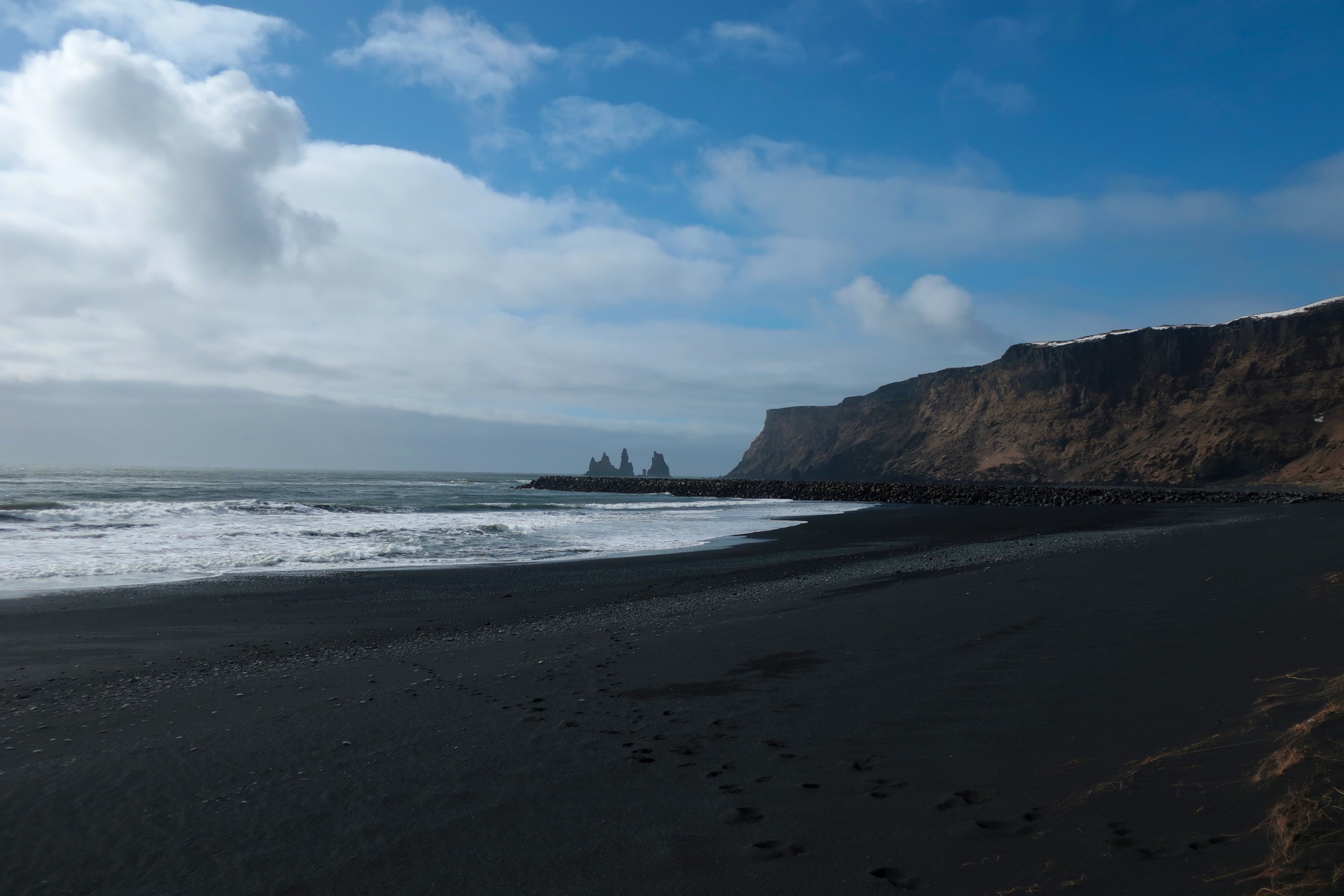 Black Sand Beach of Vik Iceland with Cliffs, Water, a blue sky a sea stack on the background