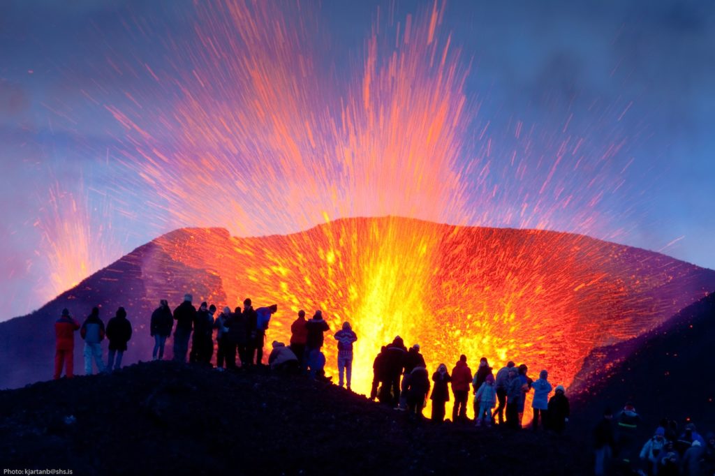 Gruppe von Menschen beobachtet aus nächster Nähe eine spektakuläre Vulkaneruption mit sprühender Lava in Island.